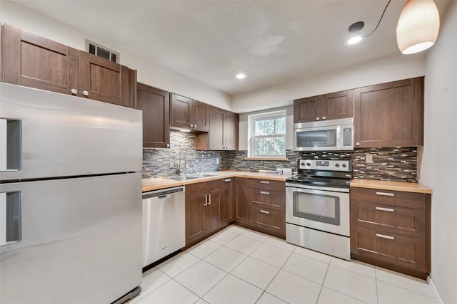 kitchen with stainless steel appliances, a sink, tasteful backsplash, light tile patterned flooring, and butcher block counters