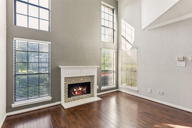 14333 Preston Rd Unit 1103, Dallas, TX 75254 - unfurnished living room featuring a textured wall, a tile fireplace, a high ceiling, hardwood / wood-style floors, and plenty of natural light
