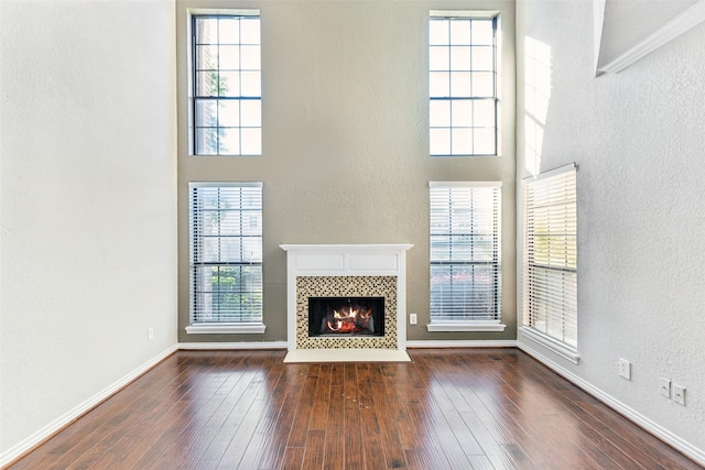 14333 Preston Rd Unit 1103, Dallas, TX 75254 - unfurnished living room featuring a tiled fireplace, wood-type flooring, a high ceiling, baseboards, and a textured wall