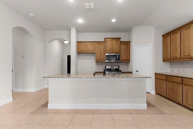 1105 Pigeon Hawk Dr, Little Elm, TX 75068 - kitchen featuring stainless steel appliances, brown cabinetry, arched walkways, decorative backsplash, and recessed lighting