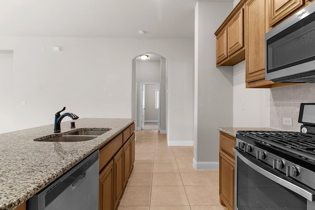 1105 Pigeon Hawk Dr, Little Elm, TX 75068 - kitchen with stainless steel appliances, a sink, arched walkways, light stone counters, and brown cabinetry