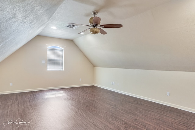 additional living space featuring ceiling fan, dark wood-style floors, vaulted ceiling, baseboards, and a textured ceiling