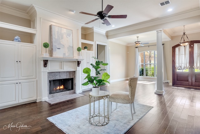 living room with decorative columns, ceiling fan, dark wood finished floors, a tiled fireplace, and baseboards