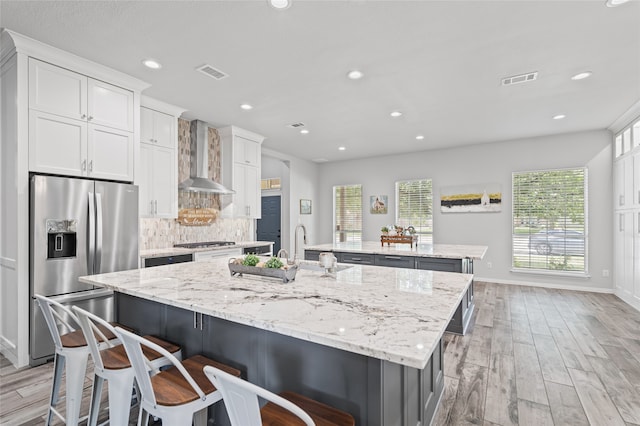 1701 Travis Ct, Allen, TX 75002 - kitchen with appliances with stainless steel finishes, an island with sink, wall chimney range hood, light wood-type flooring, and baseboards