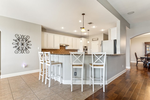 1250 Amistad Dr, Prosper, TX 75078 - kitchen with freestanding refrigerator, arched walkways, a breakfast bar area, tasteful backsplash, and dark stone counters