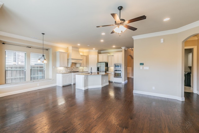 unfurnished living room with arched walkways, a ceiling fan, ornamental molding, dark wood finished floors, and a sink