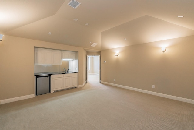 kitchen featuring vaulted ceiling, light colored carpet, baseboards, white cabinets, and refrigerator