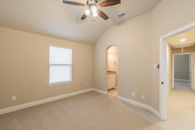unfurnished bedroom with attic access, light colored carpet, arched walkways, vaulted ceiling, and baseboards