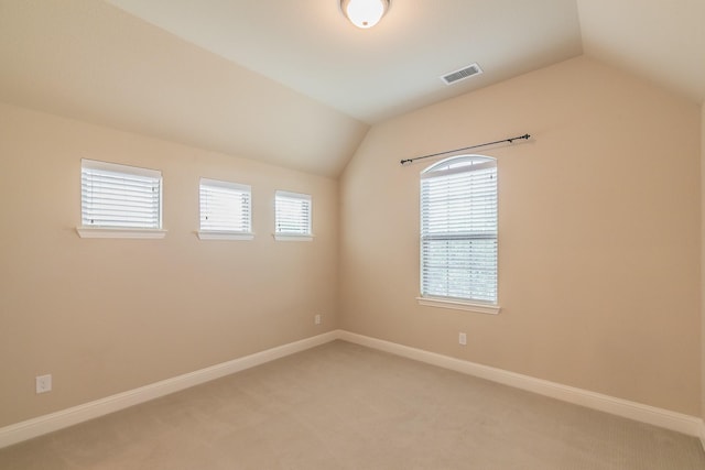 empty room featuring lofted ceiling, light carpet, healthy amount of natural light, and baseboards