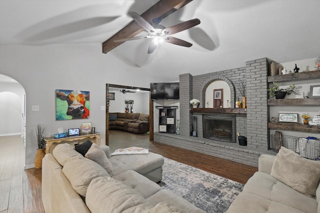 living room with a ceiling fan, arched walkways, a fireplace, wood finished floors, and baseboards