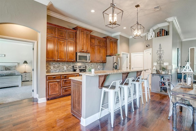 9001 Magnolia Vale Dr, Granbury, TX 76049 - kitchen with appliances with stainless steel finishes, brown cabinets, ornamental molding, a breakfast bar area, and a kitchen island with sink