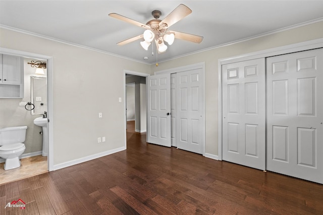 unfurnished bedroom with multiple closets, dark wood-style flooring, ornamental molding, baseboards, and ensuite bathroom