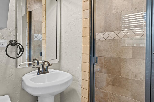 bathroom featuring a sink, a stall shower, and a textured wall