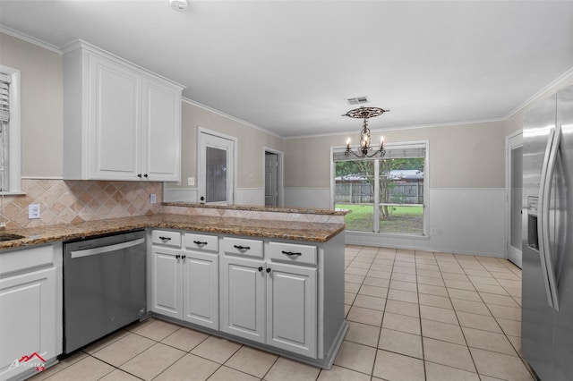 kitchen with stainless steel appliances, light tile patterned floors, white cabinets, a chandelier, and a wainscoted wall