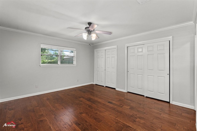 unfurnished bedroom with two closets, crown molding, baseboards, dark wood finished floors, and a ceiling fan