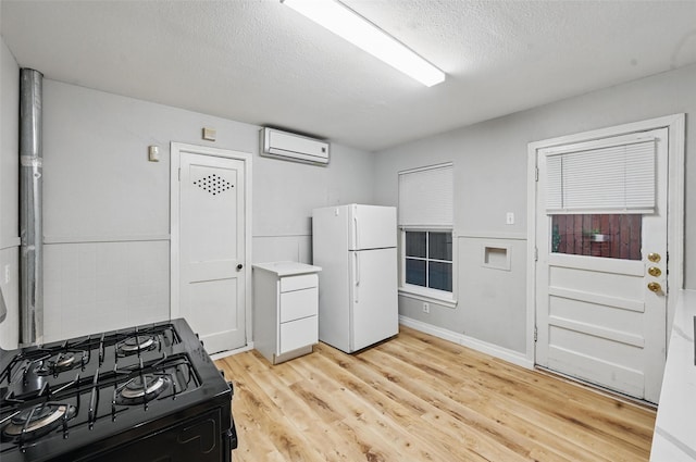4808 Birchman Ave, Fort Worth, TX 76107 - kitchen featuring freestanding refrigerator, light wood finished floors, a wall mounted air conditioner, a textured ceiling, and black gas stove