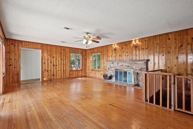 219 Ray Rd, Pottsboro, TX 75076 - unfurnished living room featuring a textured ceiling, ceiling fan, wooden walls, hardwood / wood-style floors, and a fireplace