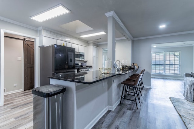 2801 Peachtree Ln, Pantego, TX 76013 - kitchen with stainless steel appliances, white cabinetry, a breakfast bar, a barn door, and light wood-type flooring