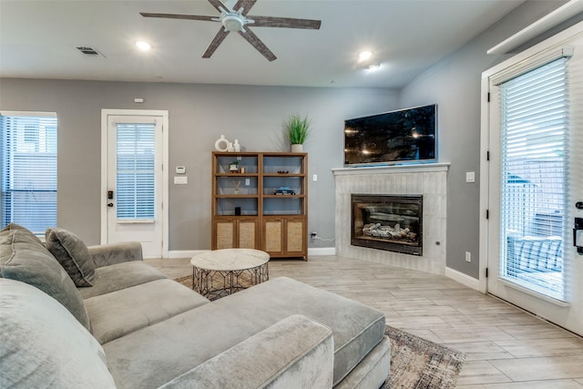 5006 Mission Ave, Dallas, TX 75206 - living room featuring ceiling fan, a tiled fireplace, baseboards, light wood finished floors, and plenty of natural light