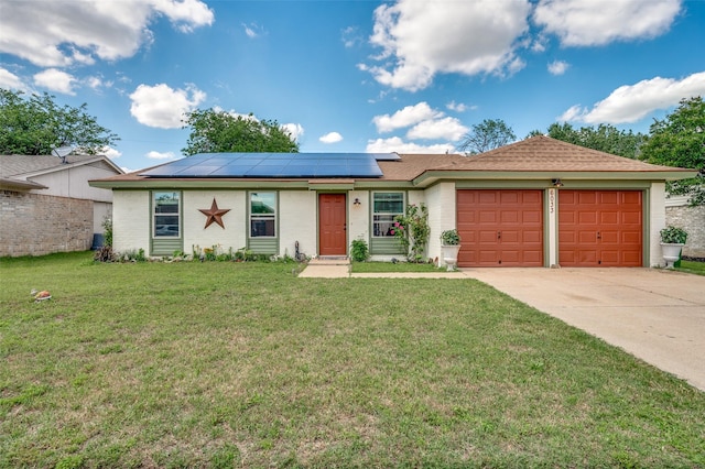 ranch-style home featuring an attached garage, driveway, solar panels, a front yard, and brick siding