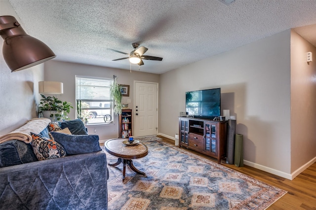 living area with a ceiling fan, wood finished floors, baseboards, and a textured ceiling