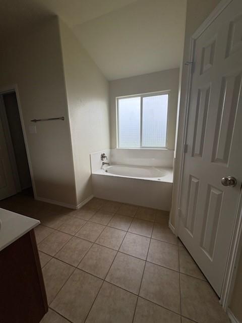 10237 Marigold Rd, Waco, TX 76708 - bathroom featuring tile patterned floors, a bath, vaulted ceiling, vanity, and baseboards