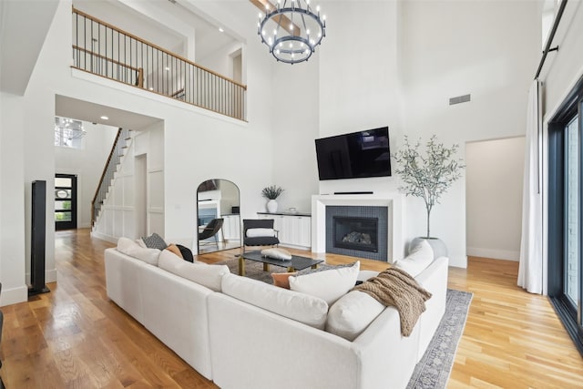 living area with a high ceiling, a fireplace, stairs, wood finished floors, and a chandelier