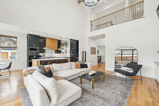 living room with a high ceiling, light wood-style flooring, baseboards, and a chandelier