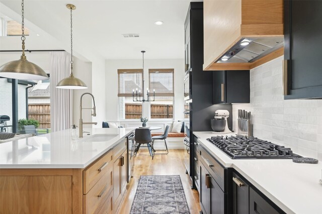 kitchen with a sink, light countertops, light wood-type flooring, a chandelier, and wall chimney exhaust hood