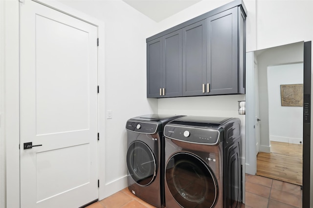 clothes washing area with independent washer and dryer, baseboards, light tile patterned floors, and cabinet space