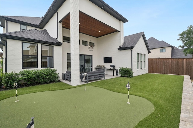 rear view of house featuring an area to practice putting, a patio, an outdoor hangout area, brick siding, and roof with shingles