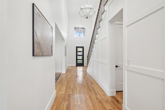 hall featuring a chandelier, stairs, light wood-style floors, baseboards, and a towering ceiling