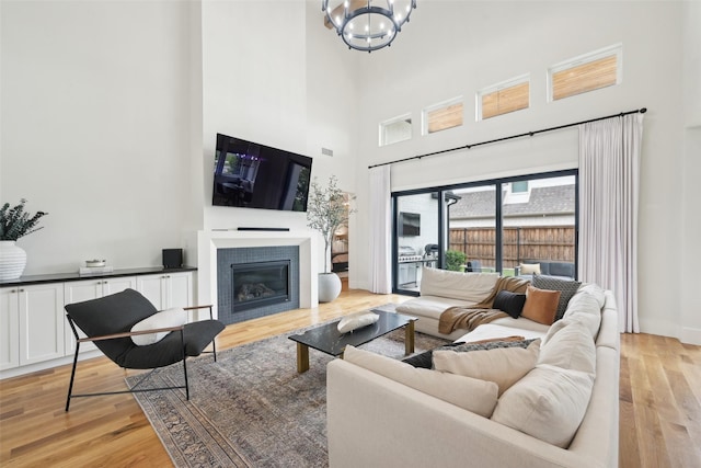 living area with a towering ceiling, light wood-style flooring, a tile fireplace, and a chandelier