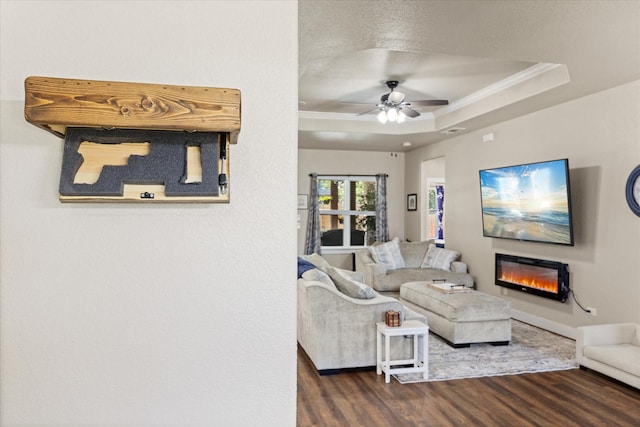 2610 Austin Dr, Granbury, TX 76048 - living area featuring dark wood-style flooring, a glass covered fireplace, crown molding, a raised ceiling, and a ceiling fan