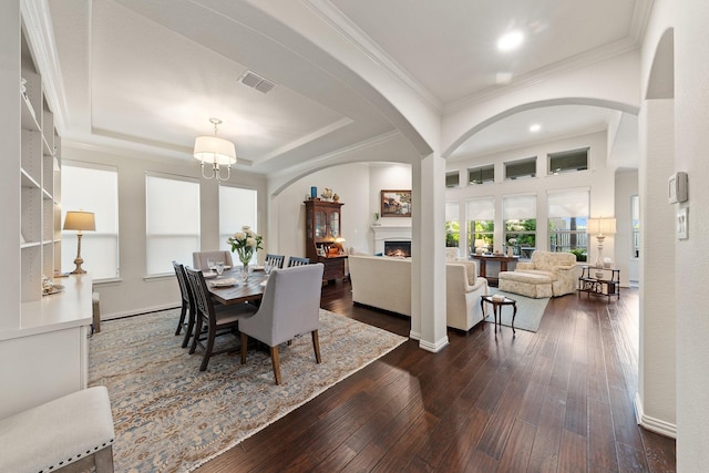 14322 Summerwoods Ln, Frisco, TX 75035 - dining room featuring a lit fireplace, dark wood-style flooring, arched walkways, crown molding, and a raised ceiling