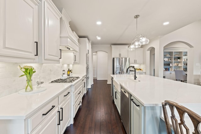 14322 Summerwoods Ln, Frisco, TX 75035 - kitchen featuring appliances with stainless steel finishes, arched walkways, light countertops, dark wood-style flooring, and custom exhaust hood