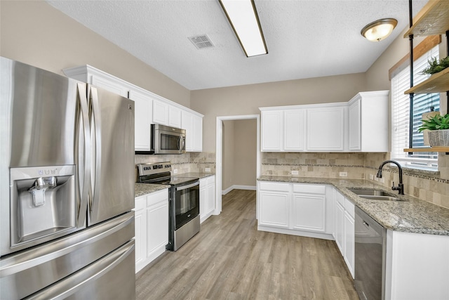 207 Trailwood Dr, Allen, TX 75002 - kitchen featuring stainless steel appliances, a sink, light wood-style floors, tasteful backsplash, and white cabinetry