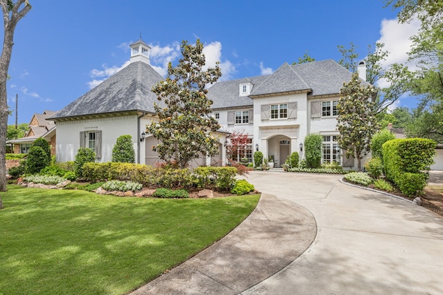 french provincial home with a chimney, a front yard, and concrete driveway