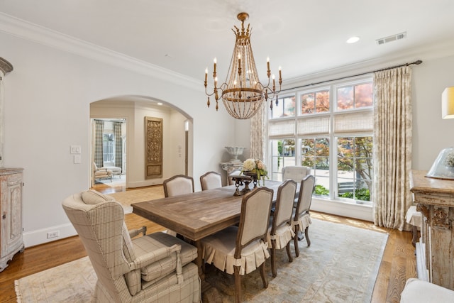 dining room with arched walkways, a chandelier, crown molding, light wood finished floors, and baseboards