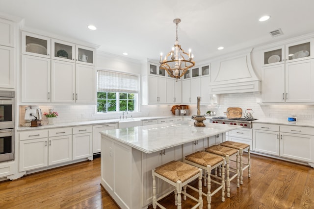 kitchen featuring premium range hood, a chandelier, a center island, decorative backsplash, and a breakfast bar area