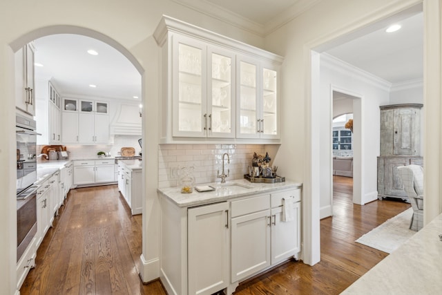 bar area with arched walkways, dark wood-style floors, a sink, crown molding, and backsplash