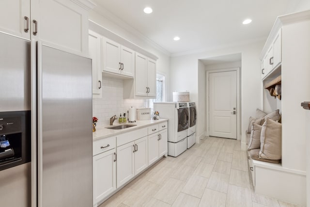 kitchen with stainless steel fridge with ice dispenser, washing machine and clothes dryer, a sink, light countertops, and white cabinets