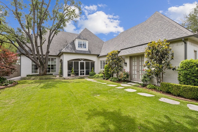 rear view of house featuring french doors, roof with shingles, a lawn, and a sunroom