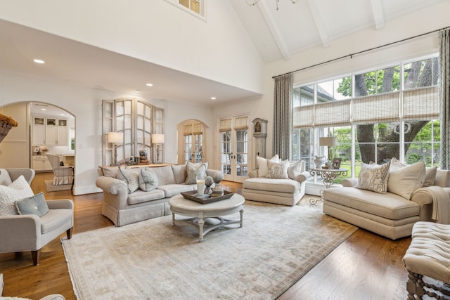 living area with arched walkways, high vaulted ceiling, beam ceiling, wood finished floors, and recessed lighting