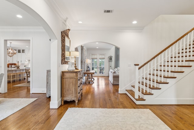 entrance foyer with arched walkways, stairway, wood finished floors, baseboards, and ornamental molding