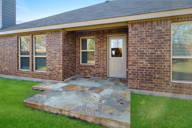 609 Racine Dr, Oak Point, TX 75068 - view of exterior entry featuring brick siding, a patio, a chimney, a yard, and a shingled roof