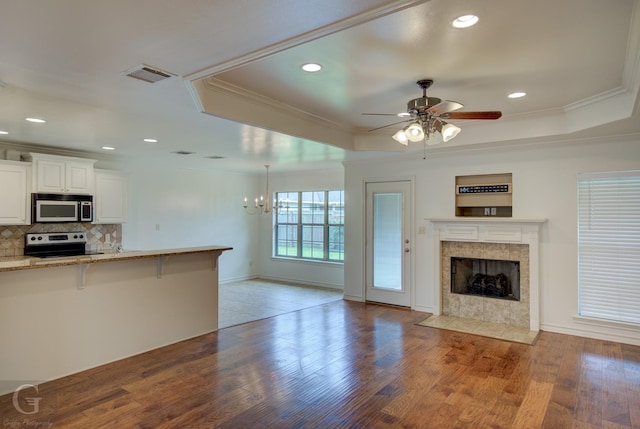 122 Lola Cir, Benton, LA 71006 - unfurnished living room with a tray ceiling, a tile fireplace, light wood finished floors, crown molding, and a ceiling fan