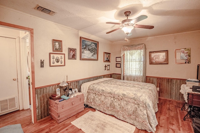 12815 N Fm 219, Dublin, TX 76446 - bedroom featuring wainscoting, light wood-style flooring, wood walls, a textured ceiling, and a ceiling fan