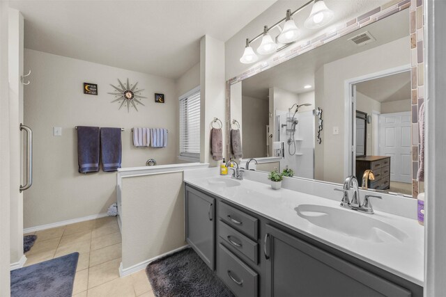 bathroom featuring a shower, double vanity, tile patterned floors, and baseboards