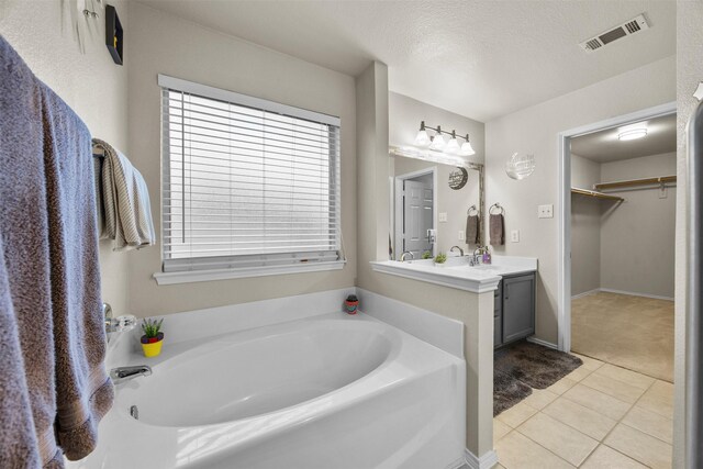 full bath with tile patterned floors, a bath, vanity, a walk in closet, and a textured ceiling